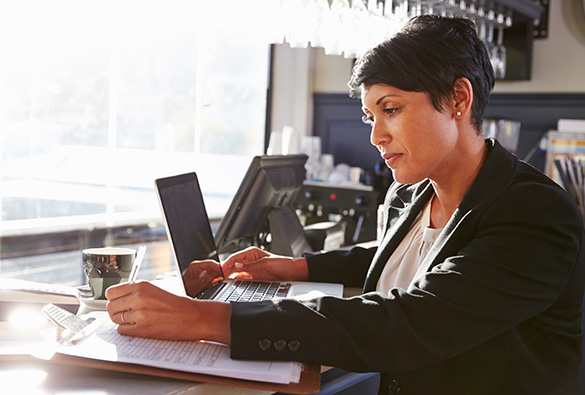 Person working on a laptop at a table with documents and a cup nearby.