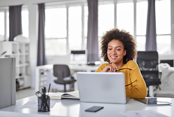 Person smiling at a laptop screen in a bright office.