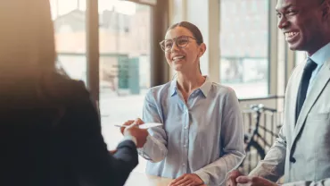 woman handing a paper to a coworker while another coworker smiles